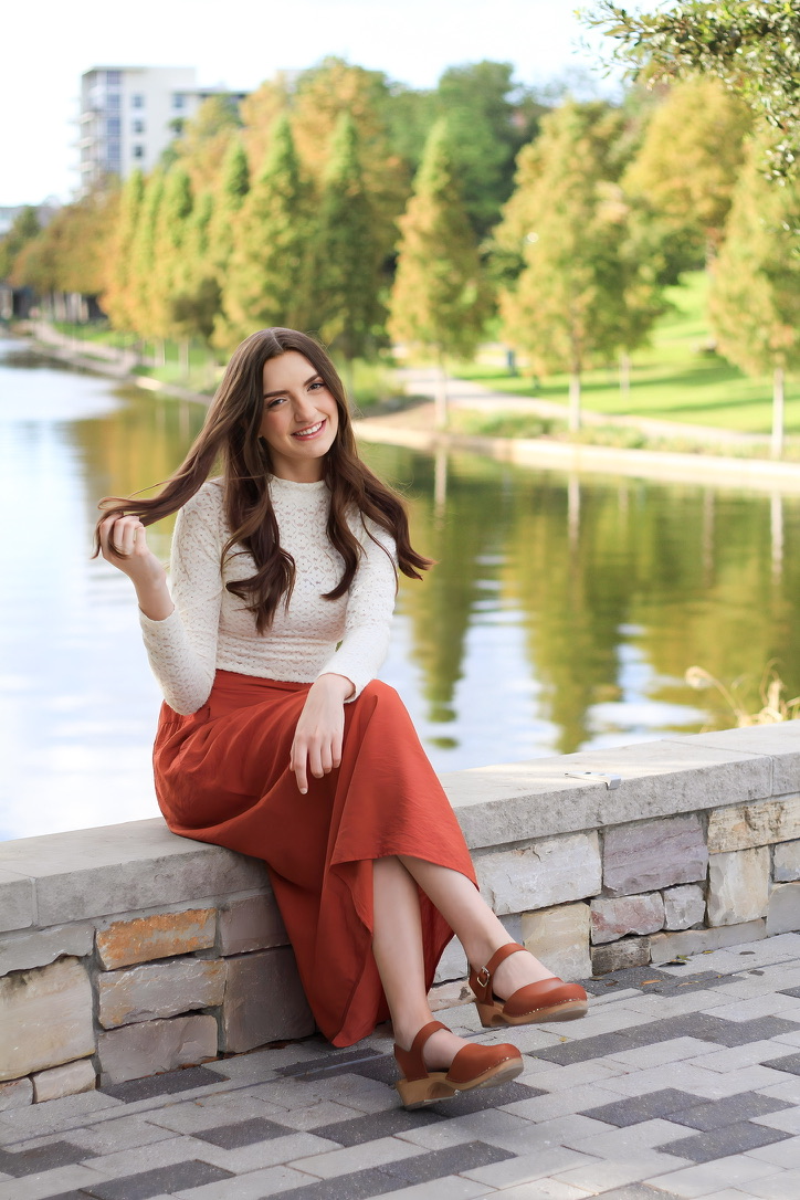 Isabelle Heath smiling, seated on a stone wall beside a pond